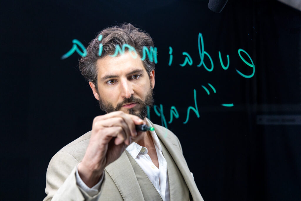 Assistant Teaching Professor of Philosophy Theodore Bergsma writes on the lightboard using a neon green marker.