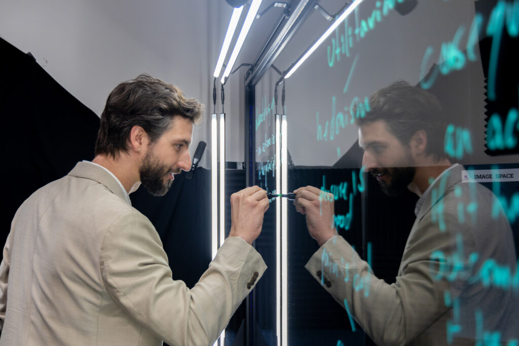 Assistant Teaching Professor of Philosophy Theodore Bergsma writes on the lightboard using a neon green marker.